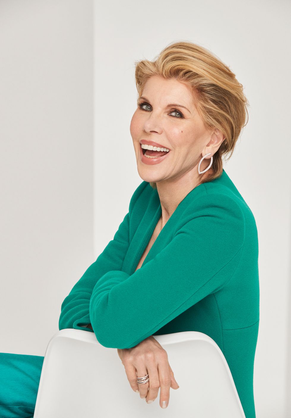 Christine Baranski in a green suit leaning against a chair.