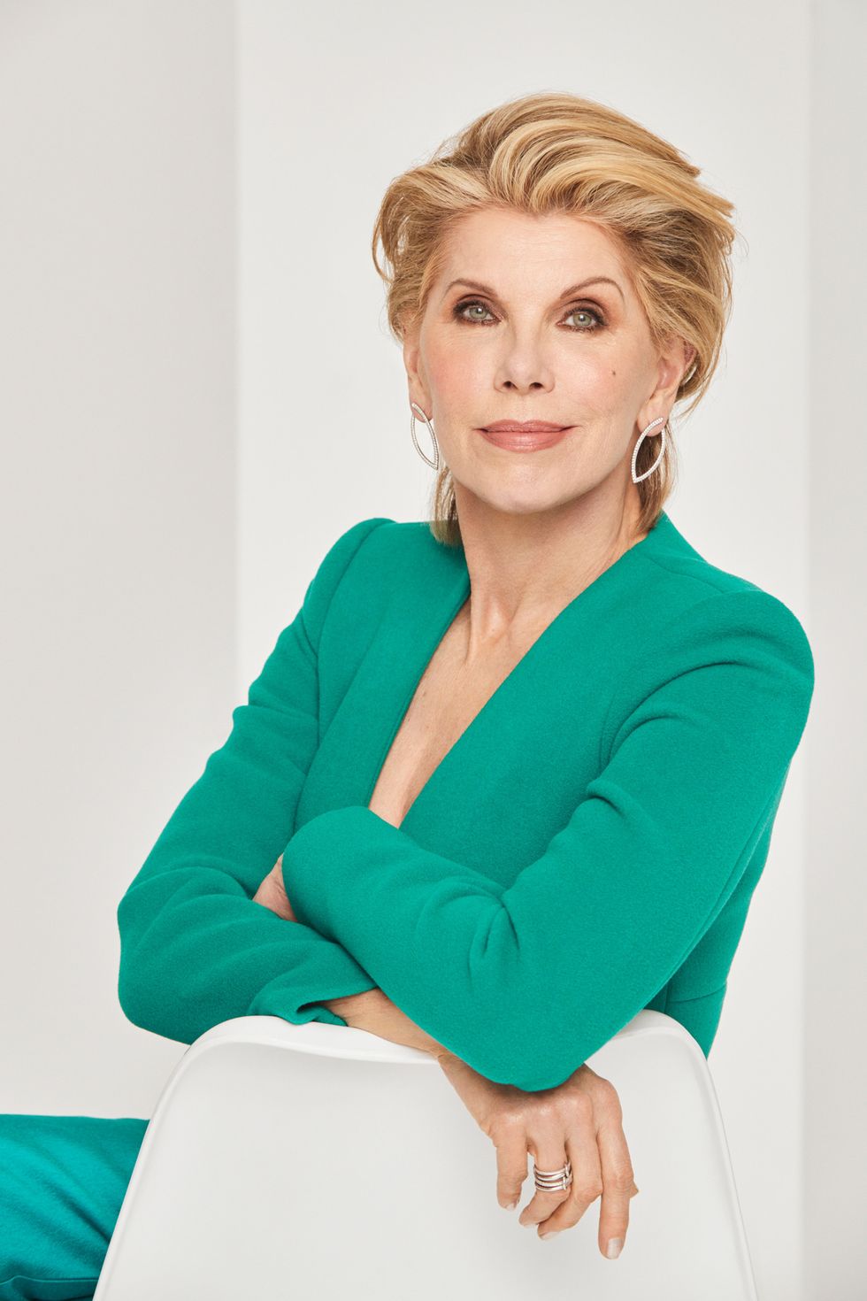 Christine Baranski in a green jacket leaning against a white chair.