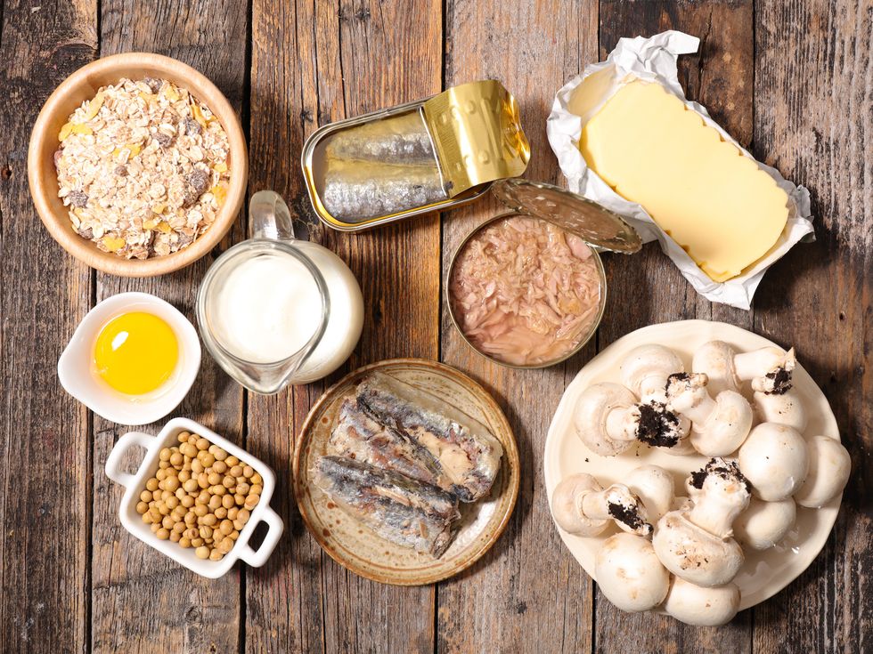 Foods high in vitamin D, including a bowl of cereal, canned herring, canned tuna, butter, mushrooms, milk, and an egg yolk.