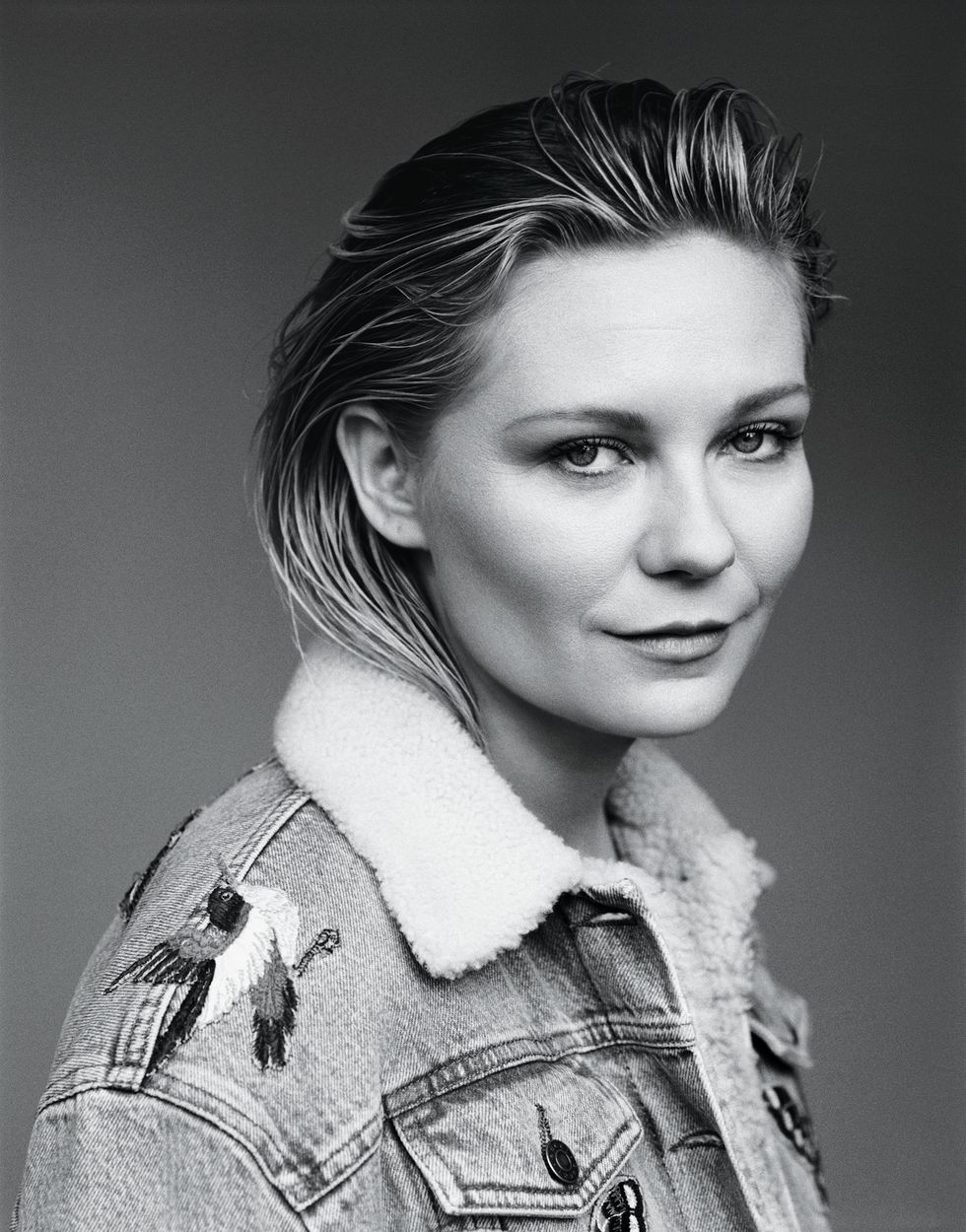 Black and white image of Kirsten Dunst smiling slyly at the camera.