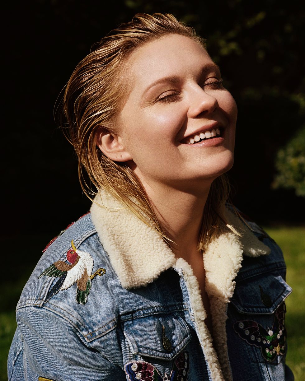 Kirsten Dunst smiles with eyes close into strong sun.