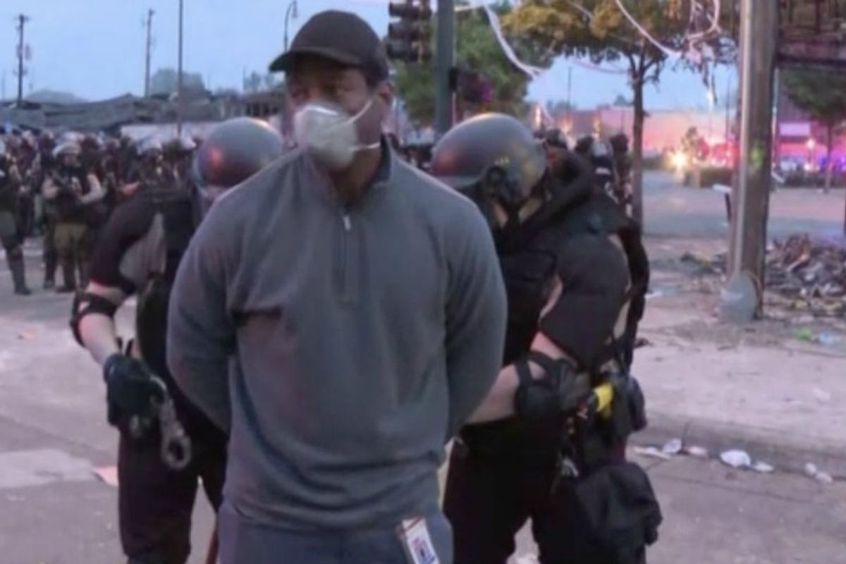 Police arresting masked man in front of a line of officers; debris visible on the street.
