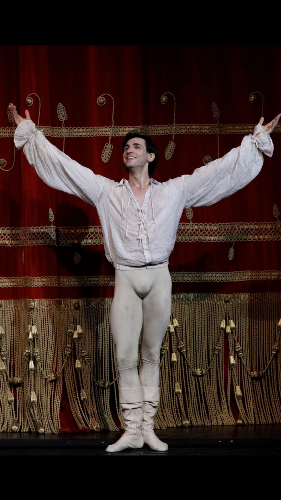 Eris Nezha, wearing a white Romeo costume, stands in front of a red and gold curtain.