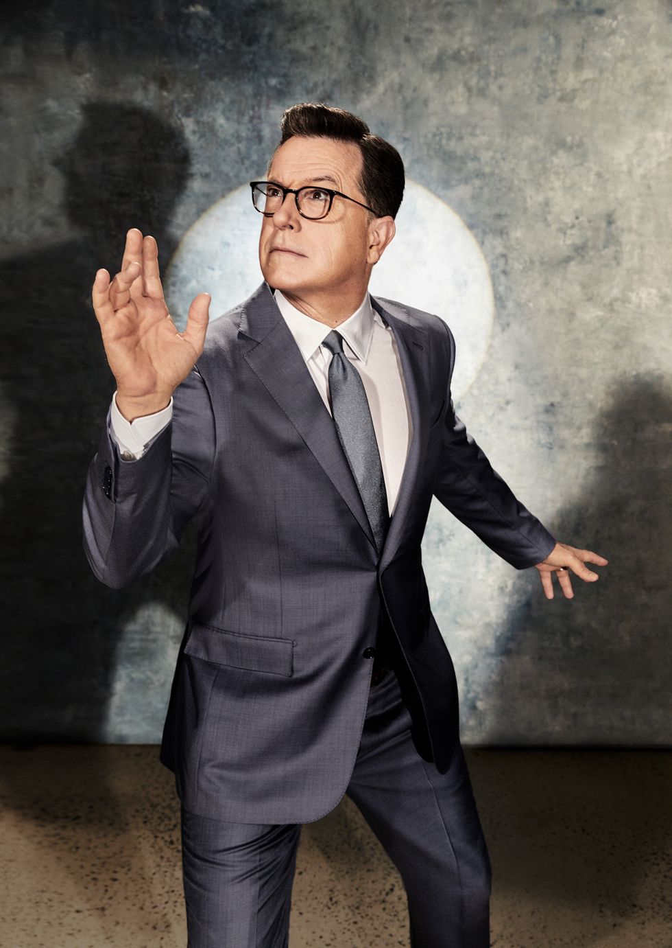Stephen Colbert in a gray suit with a spotlight behind him.