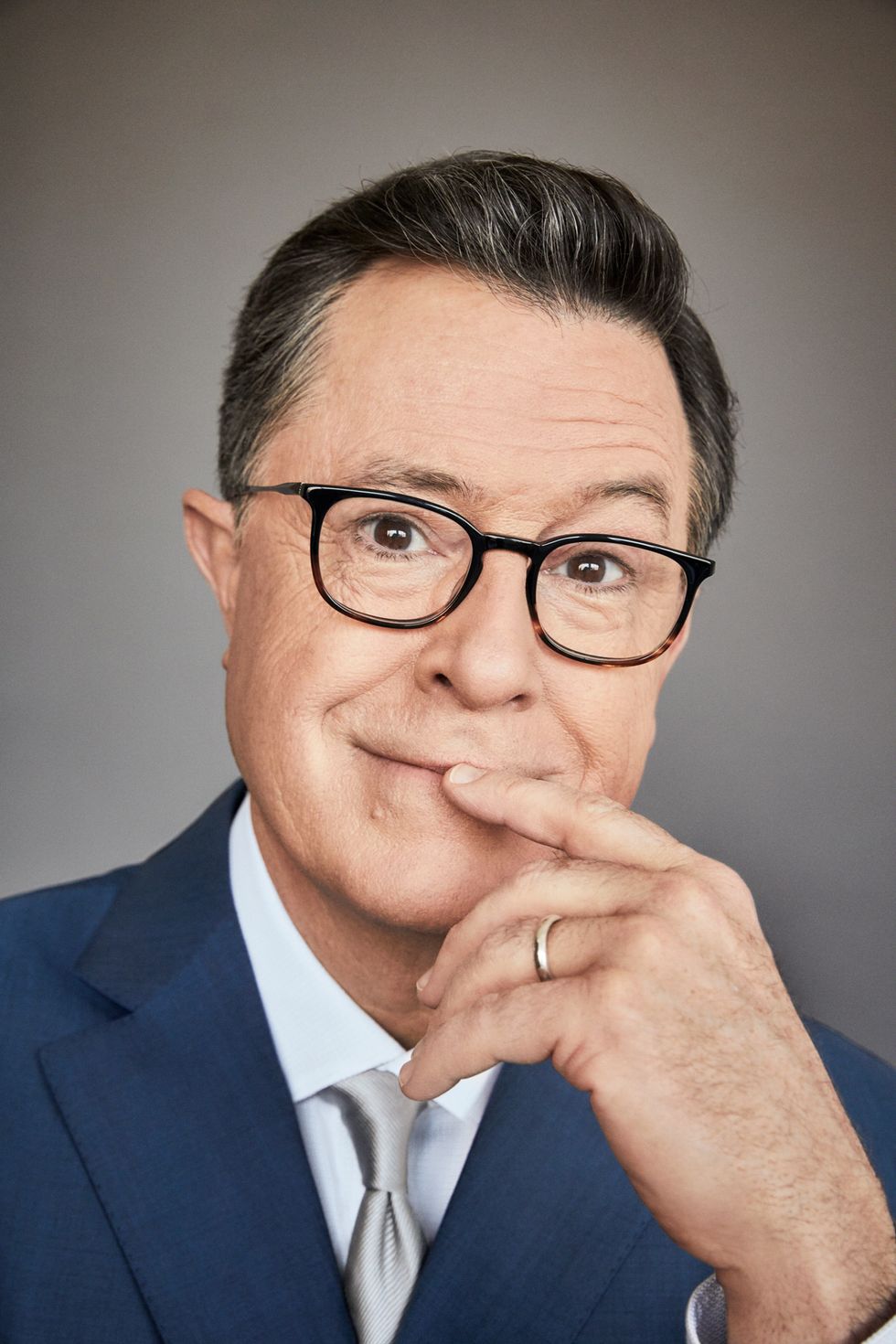 Close-up portrait of Stephen Colbert with his index finger to his lips.