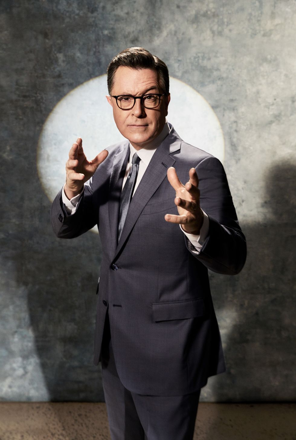 Stephen Colbert in a gray suit with a spotlight behind him.