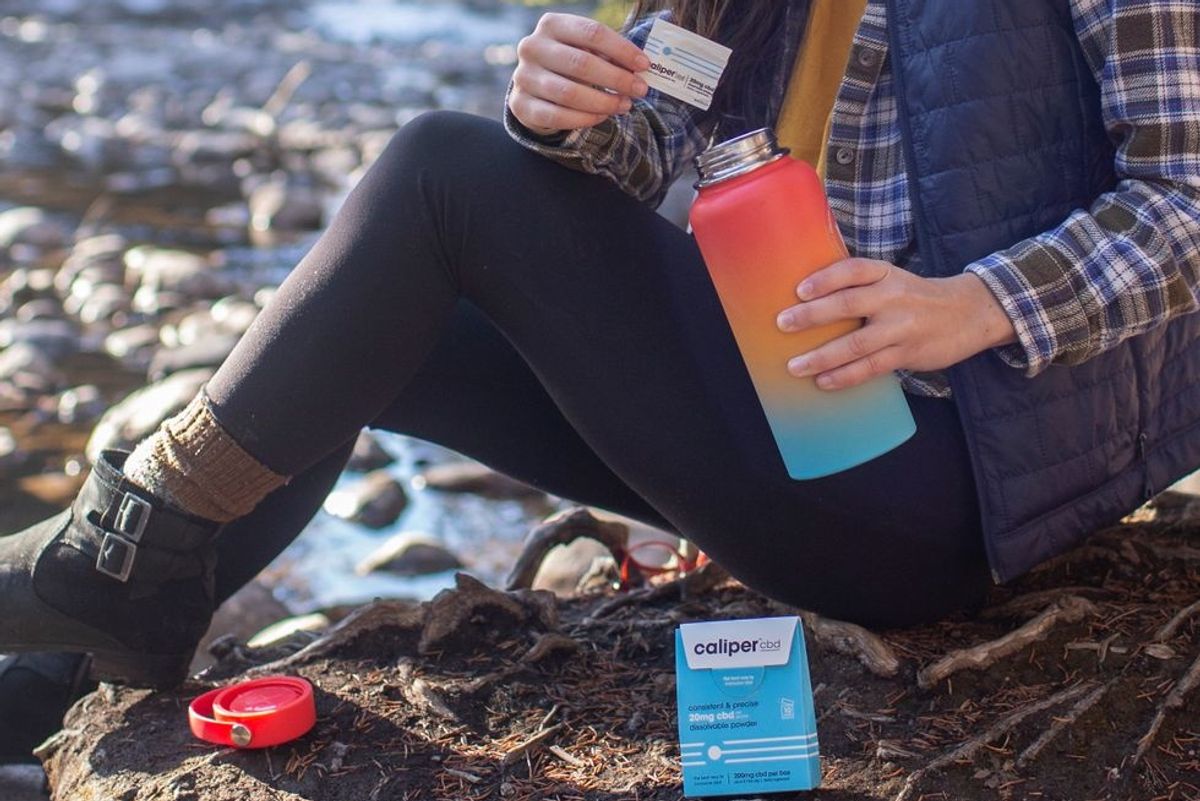 woman hiking pours a packet into brightly colored water bottle