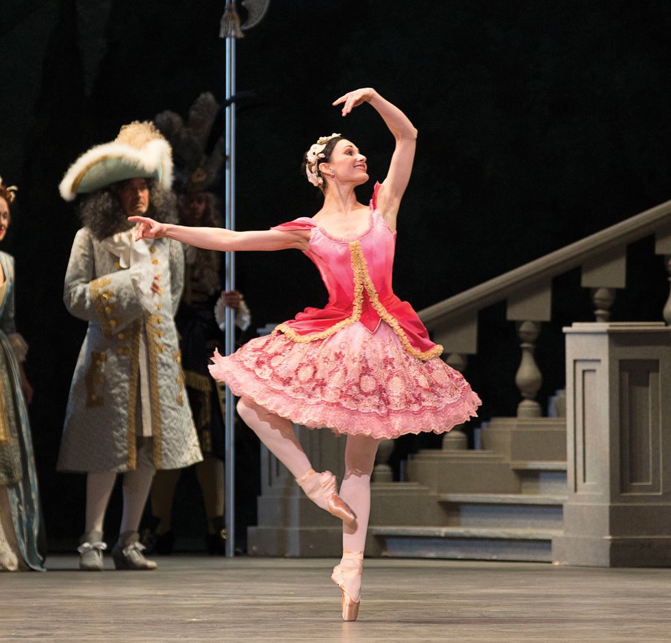 Sarah Lane in pink Aurora costume in a pass\u00e9 with one arm in the air onstage