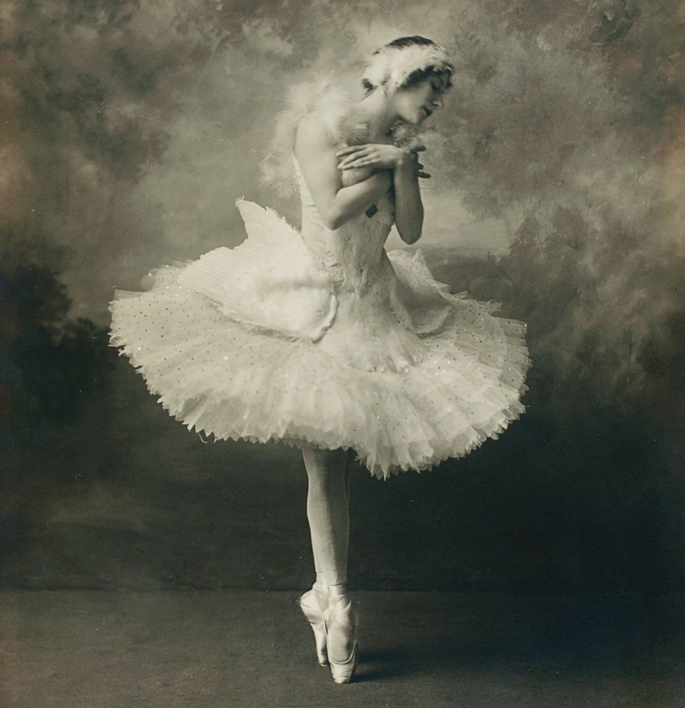 Black and white photograph of Anna Pavlova in a white swan tutu standing in fifth position on pointe with her arms crossed at her heart
