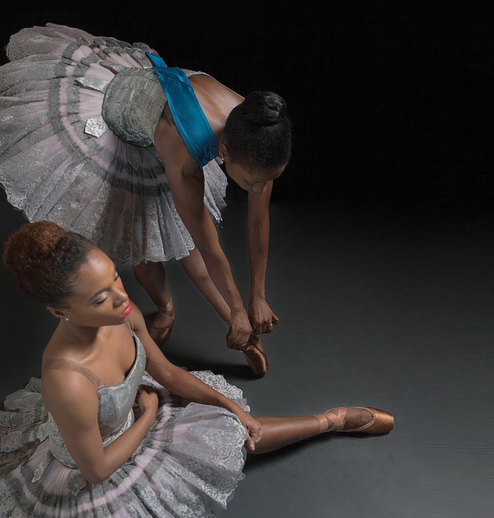 Two Black dancers in silver tutus put on satin pointe shoes