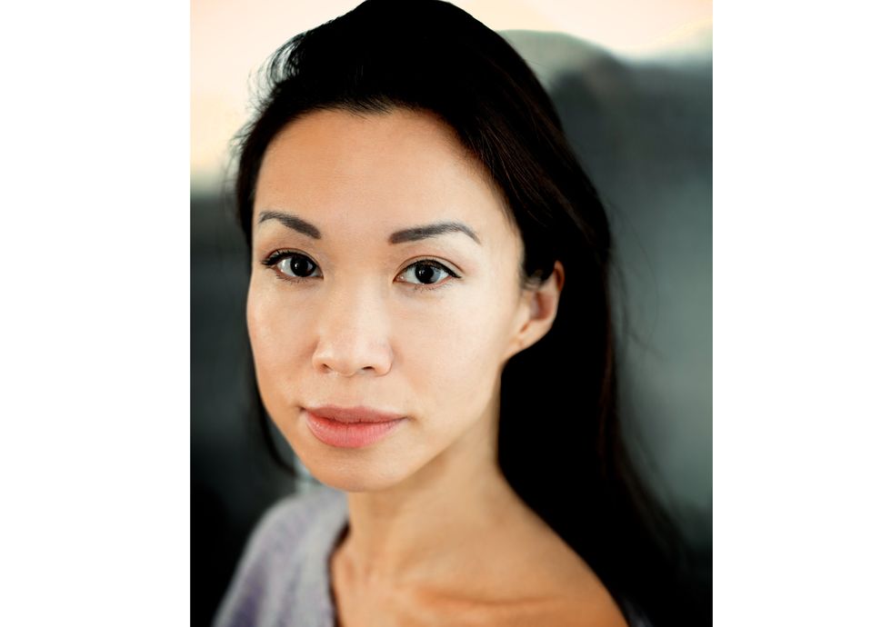long Tara Lee, wearing a wide-neck gray short and her black hair down, is shown from the neck up and smiles towards the camera.