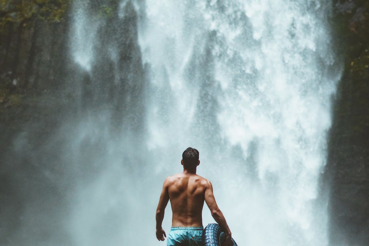 man in blue shorts in front of a waterfall