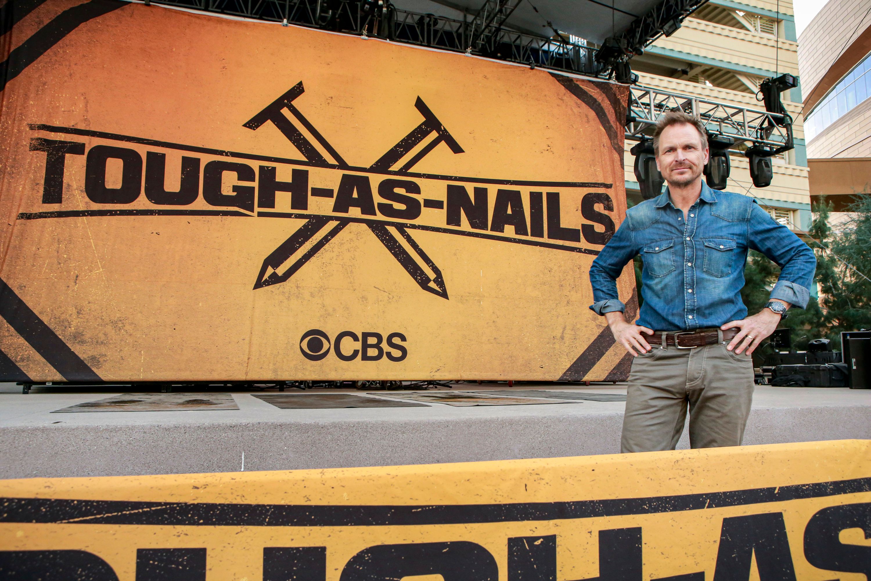 Host and executive producer Phil Keoghan in front of a large poster with the Tough As Nails logo