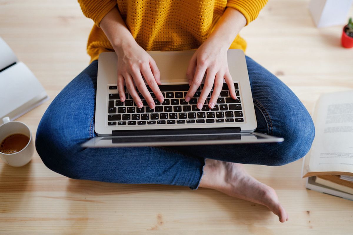 A student seated on the floor with a laptop computer