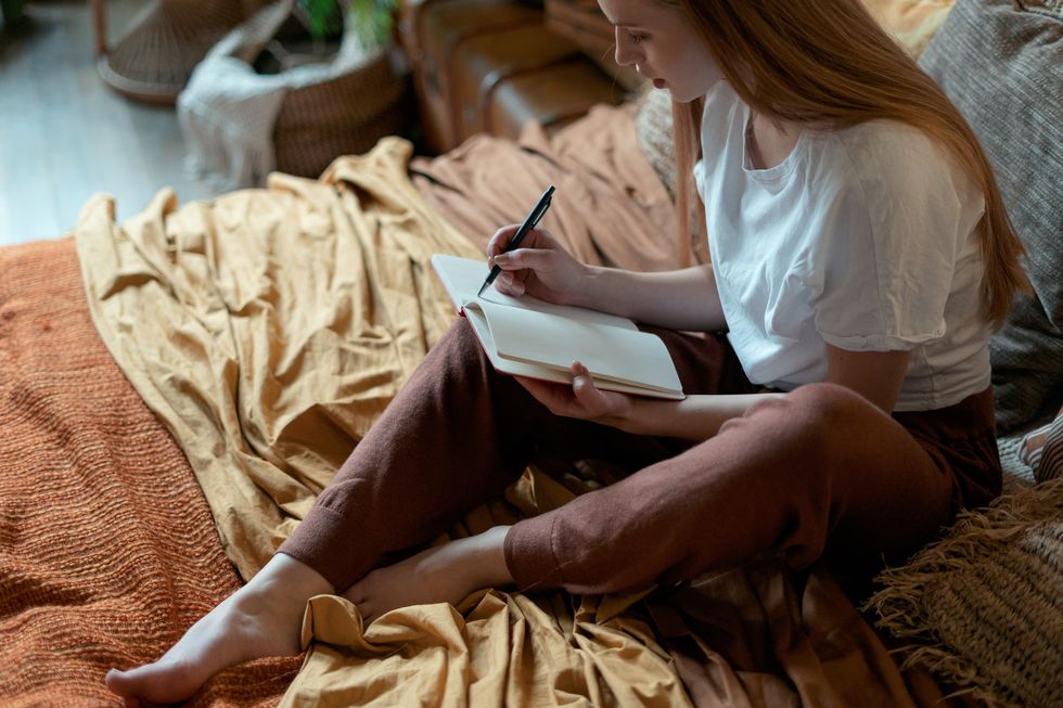 A teenage girl writes in her journal while sitting on cozy blankets.