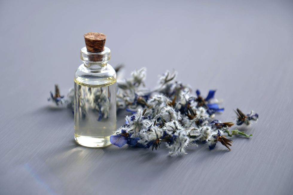 Small glass bottle of essential oil surrounded by flowers