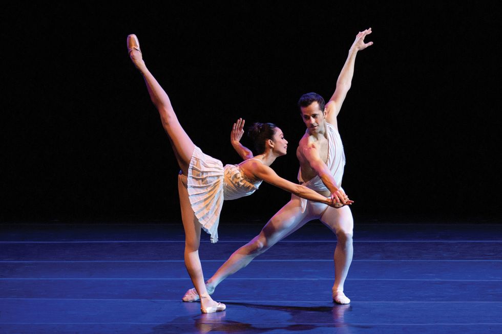 Fairchild onstage in white tights leans to the left while holding the hand of Abrera, in a pench\u00e9 in a white pleated dress.