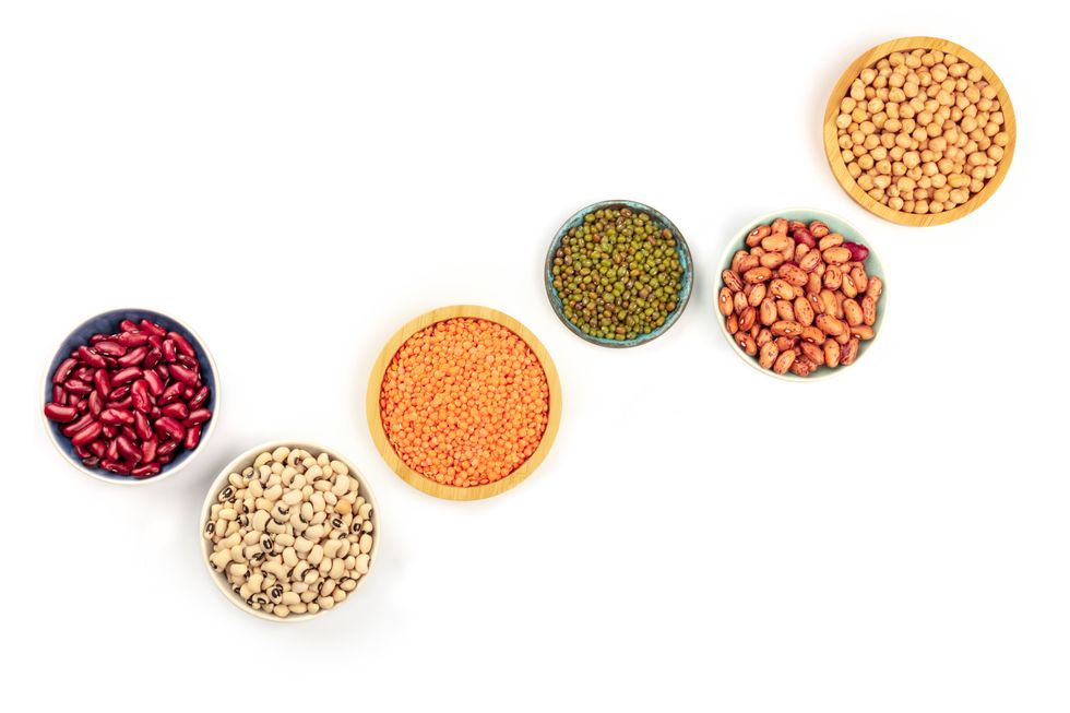 Legumes, shot from the top on a white background with copy space. Red kidney and pinto beans, lentils, chickpeas, soybeans, black eyed peas in bowls.