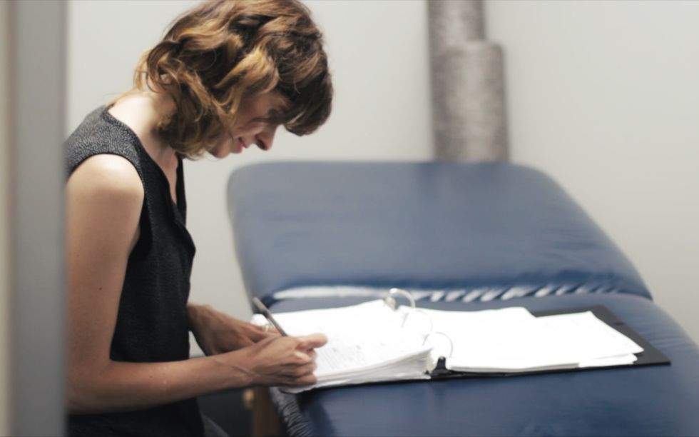 Muncrief leans over a physical therapy table, writing into a binder.