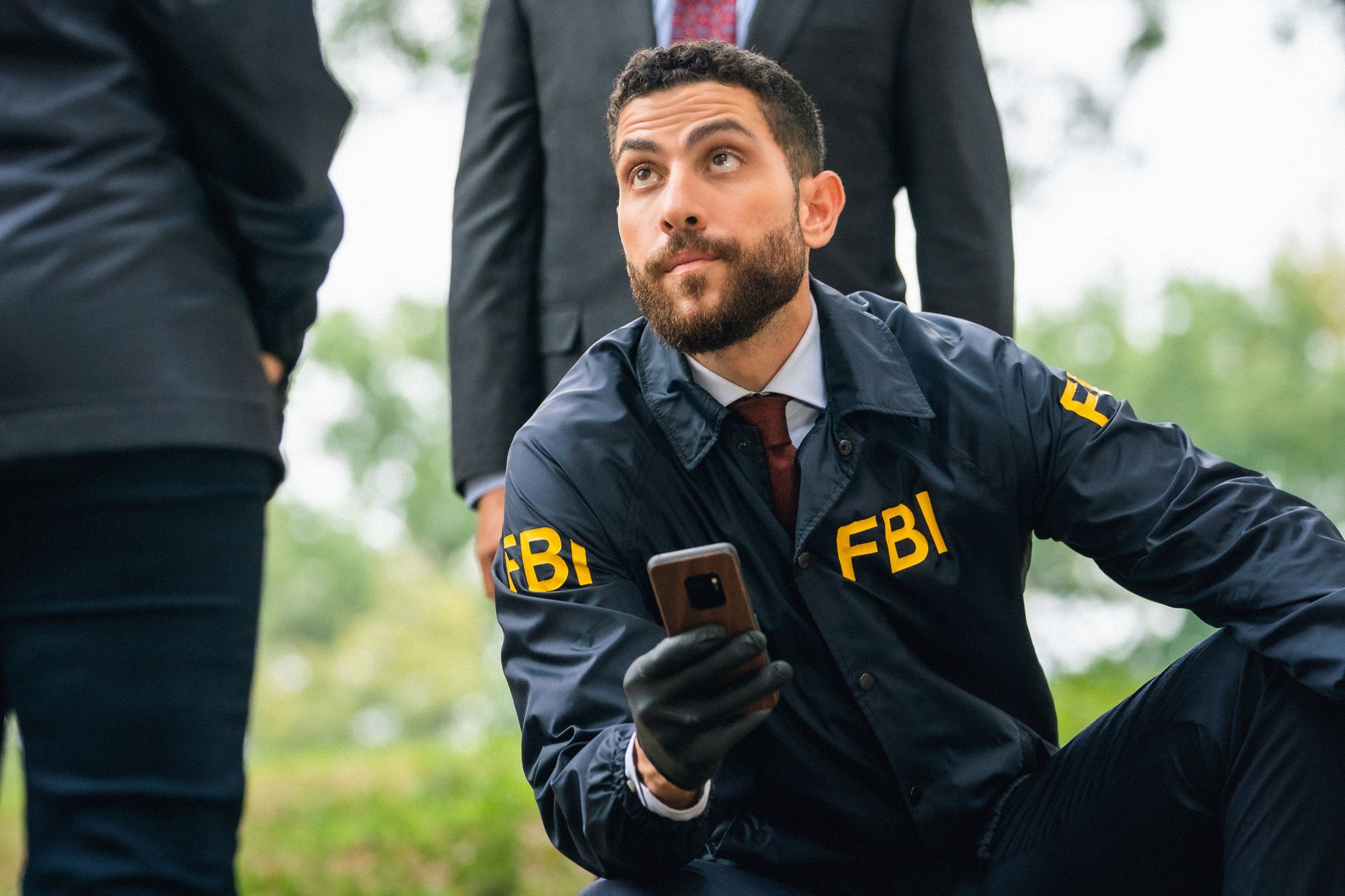 Actor Zeeko Zaki wears an FBI windbreaker while holding up a cell phone