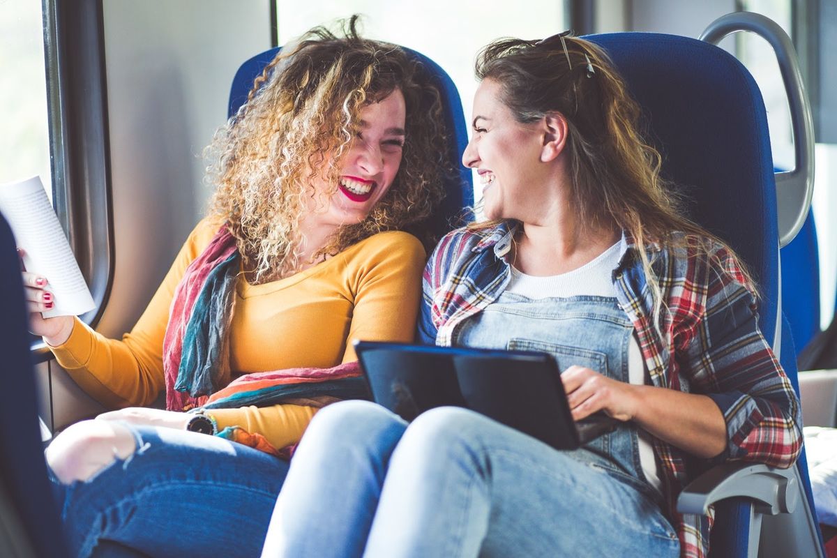 two women laughing on a train holding books 