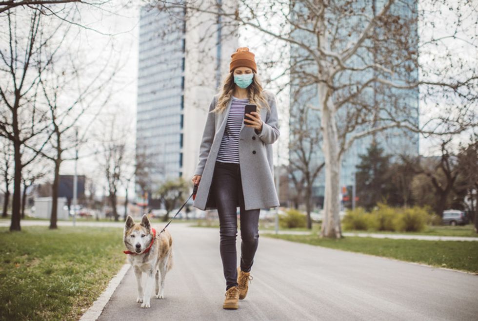 A woman holding a smartphone while walking in a mask outside