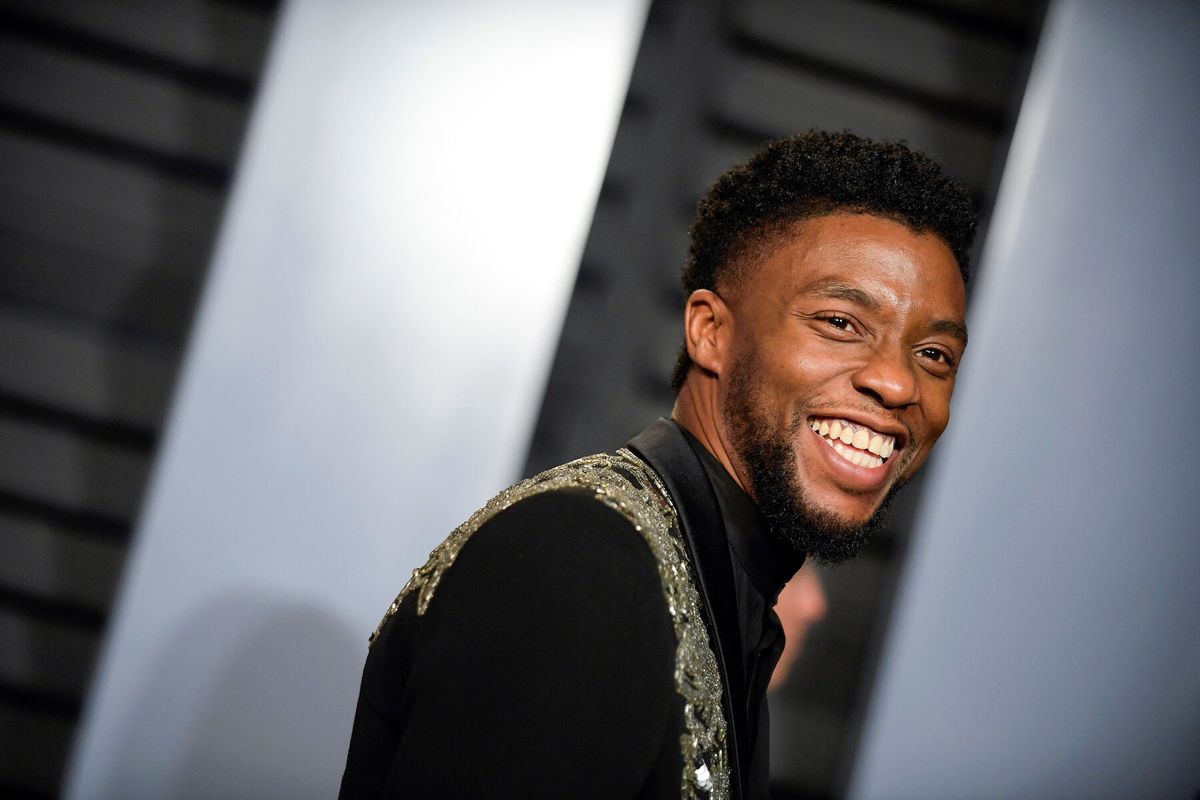 Chadwick Boseman is smiling, dressing in a black jacket with embellishment