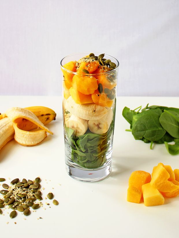 No seu liquidificador (ou copo grande, se estiver usando um liquidificador de imersão), comece espalhando o espinafre bebê, seguido da banana, da manga e depois das sementes.