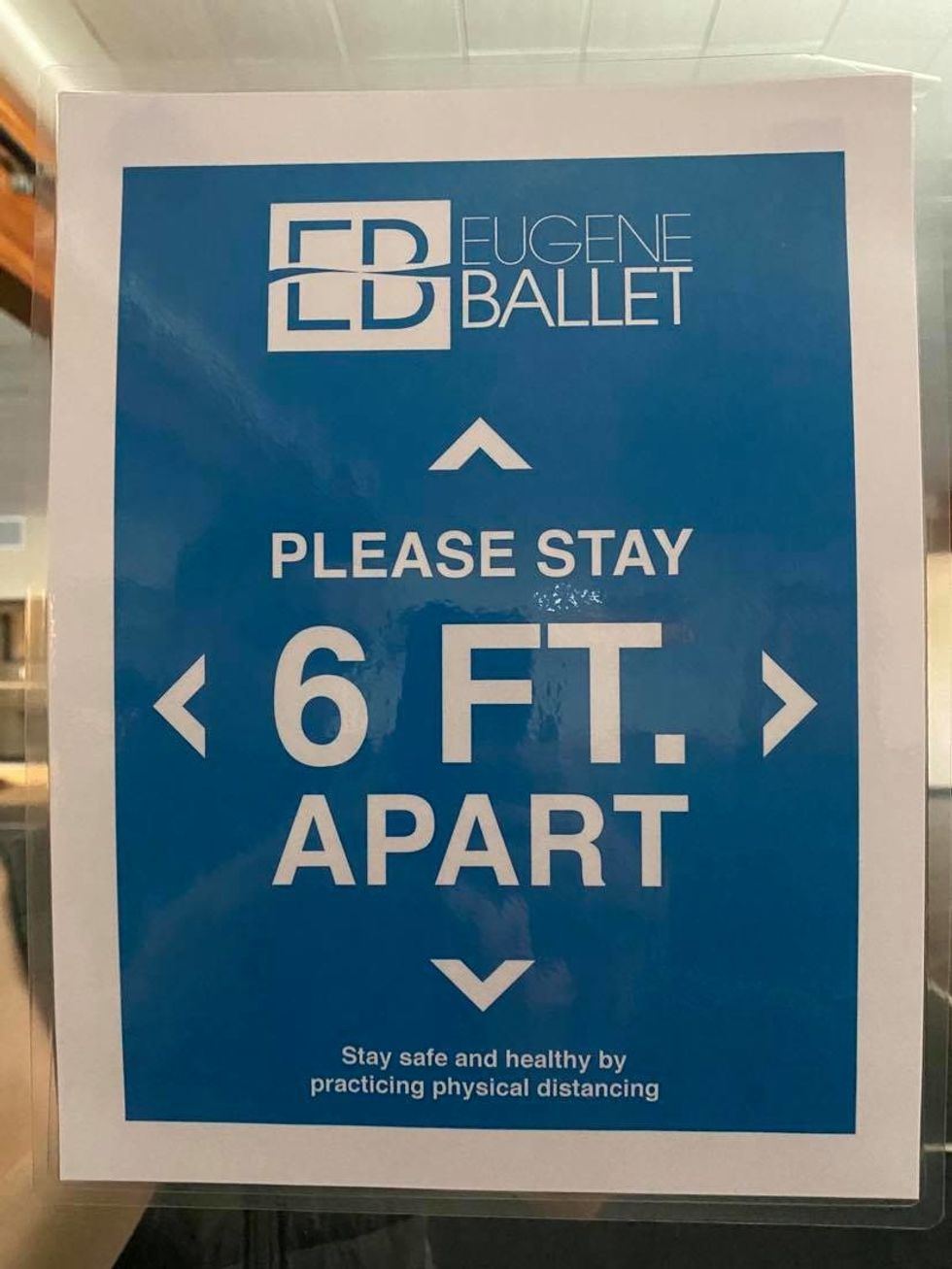 A blue sign taped to a window says "Please stay six feet apart. A pointe shoe is no longer serviceable when the shank breaks or becomes too soft to provide support. data-unit=