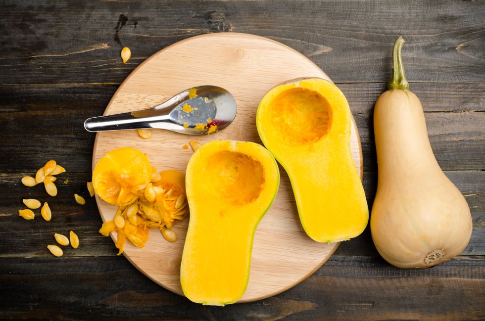 Raw butternut squash seeds next to two butternut squash halves and a whole squash