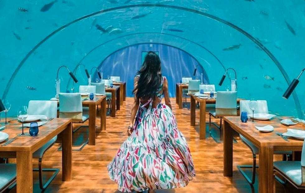 women with long dress walking through a restaurant with clear arches through which you can see the ocean