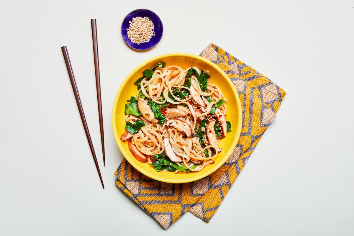 overhead shot of yellow bowl of noodles and mushrooms with yellow towel and chopsticks
