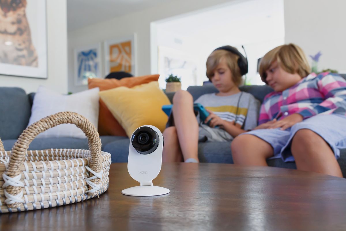 Kami Mini Indoor Camera on a coffee table with kids on a couch playing on a tablet