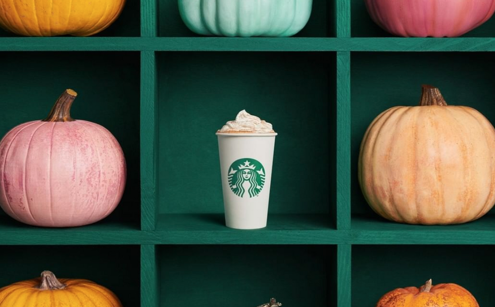 A starbucks cup on a shelf with whipped cream on it, surrounded by pumpkins