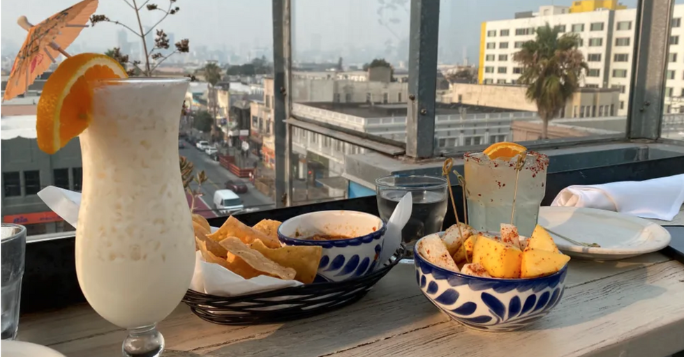 a plate and bowl of food along with two tropical drinks with a view of a city behind them