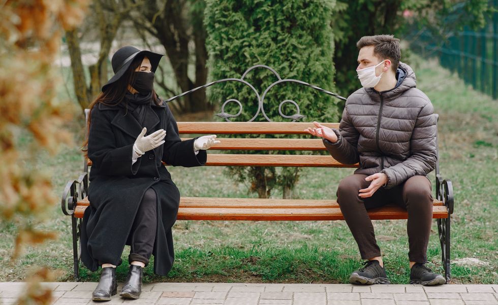 Man and woman wearing masks and chatting while social distanced on park bench