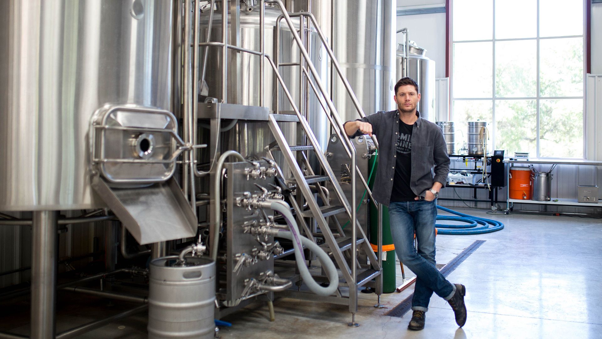 Jensen Ackles in front of beer brewing tanks