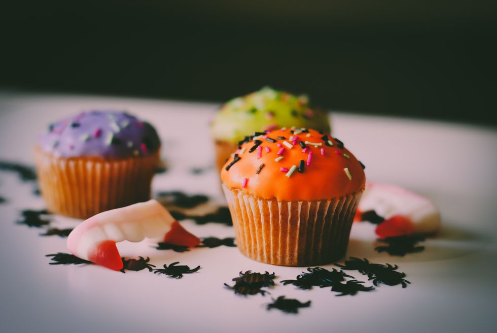 Halloween cupcakes decorated with orange, purple, and green frosting and surrounded by fake spiders and dracula teeth.