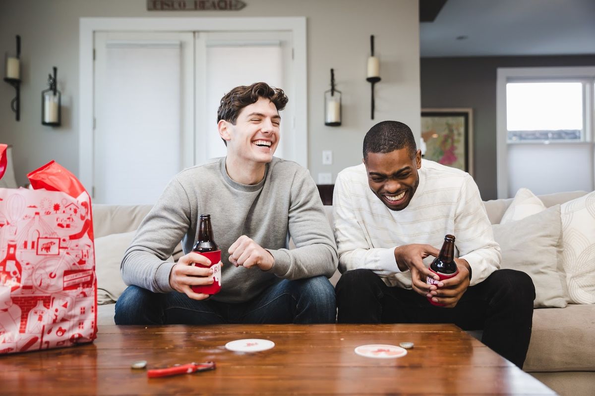 Two guys on a couch laughing and drinking beer.