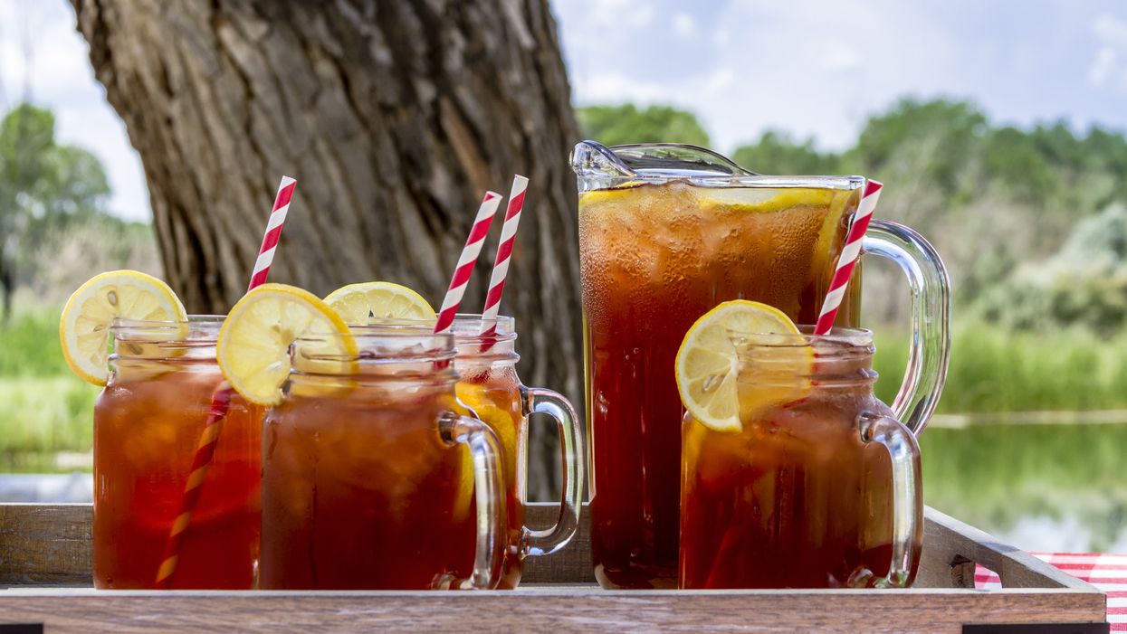 4 mason jar glasses filled with sweet tea and a lemon and a pitcher of sweet tea