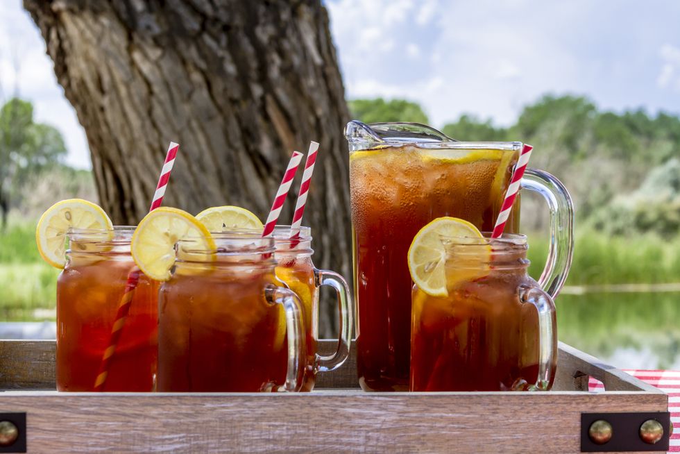 4 mason jar glasses filled with sweet tea and a lemon and a pitcher of sweet tea