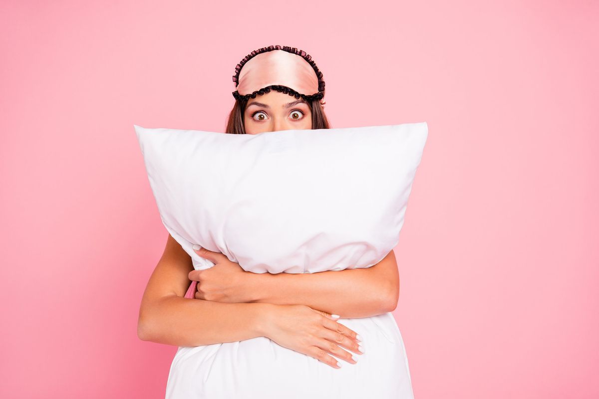 Woman hugging pillow looking surprised with a sleep mask on her head.