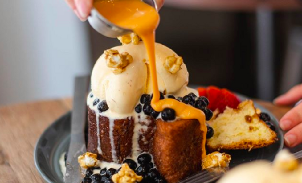 a cake topped with ice cream and bluberries with someone pouring an orange sauce over it