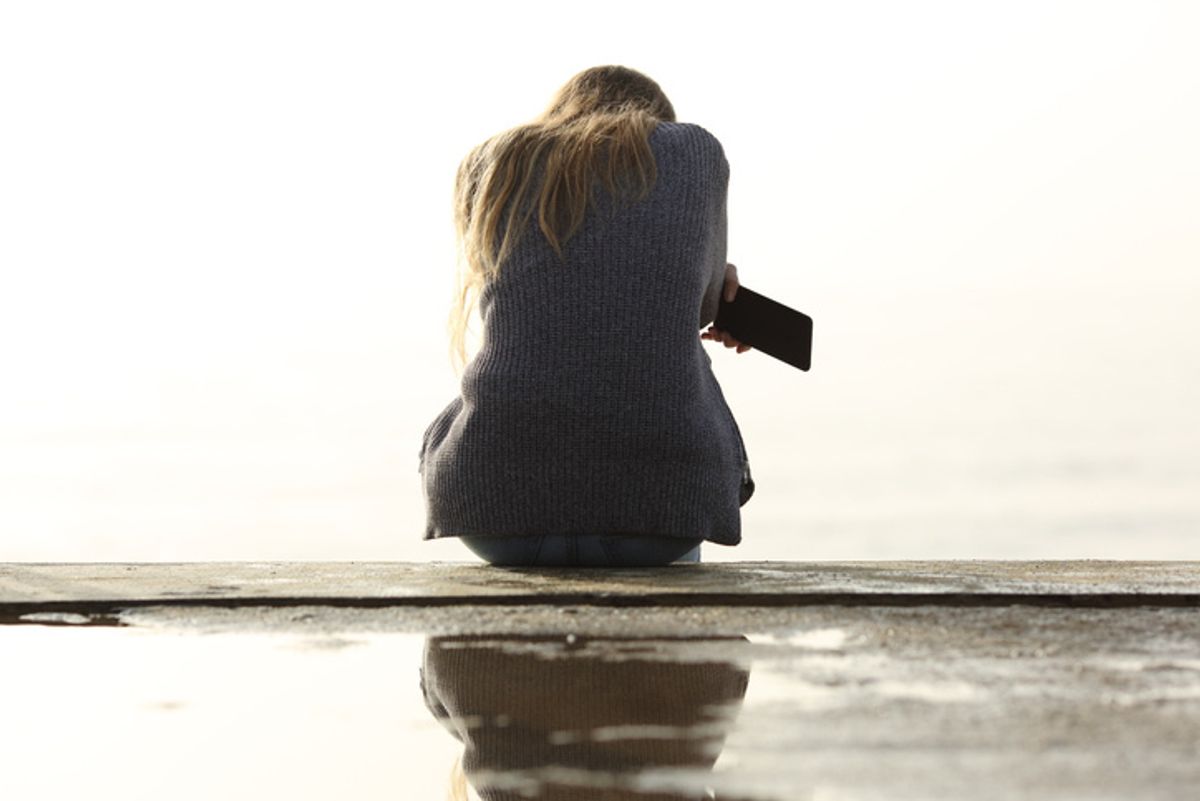 A woman seated, head down, with a smartphone in her hand