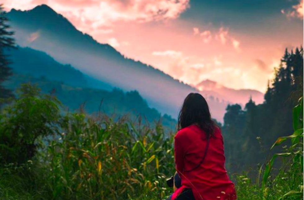 someone sitting in grass, looking out at mountain landscape