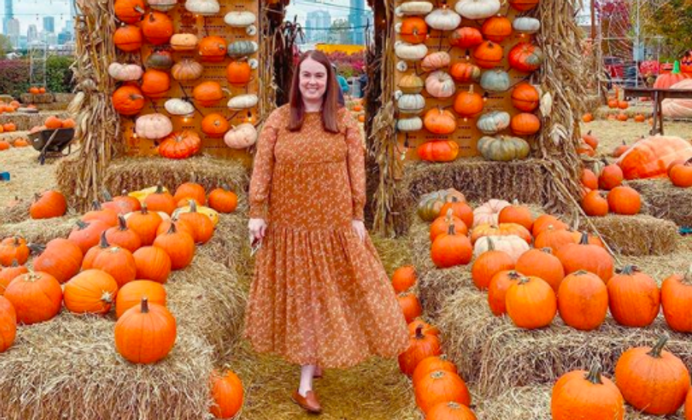 person wearing orange dress standing in front of hay and pumpkins