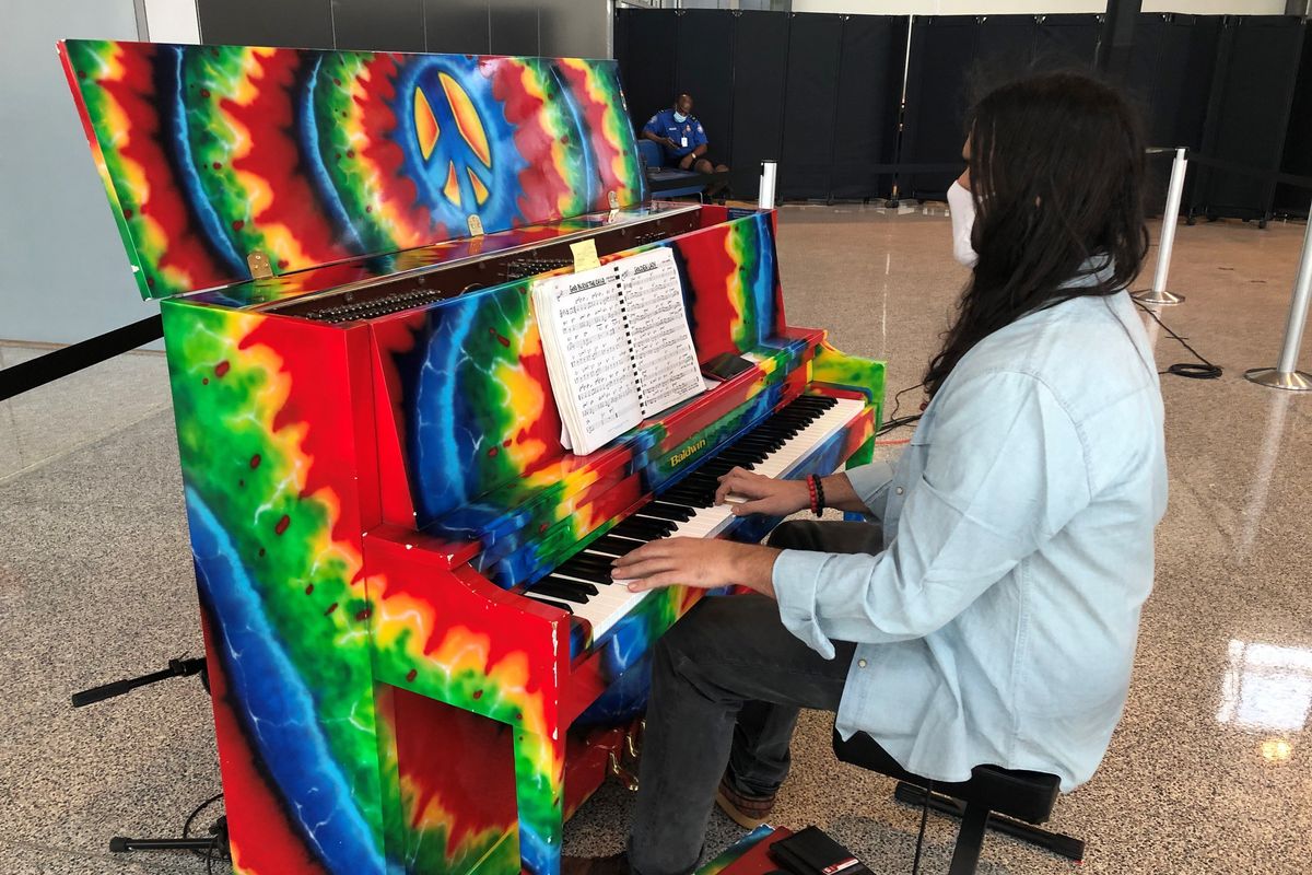Morgan sits at a rainbow tie-dye style piano in the airport.
