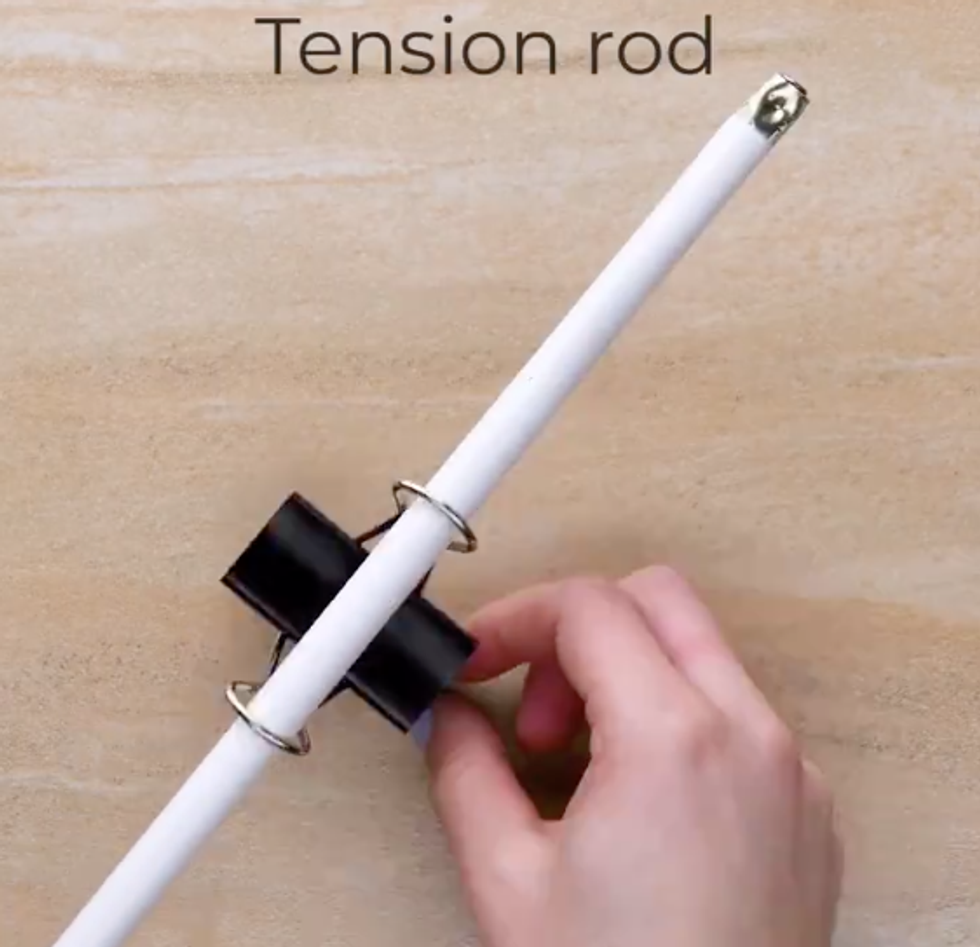 A tension rod has been pushed through the metal ends of a binder clip