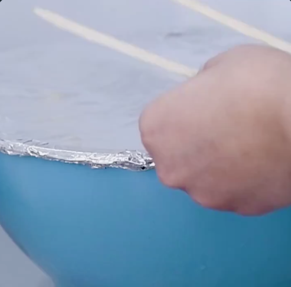 A bowl covered in tinfoil with the foil closely folded over at the edges