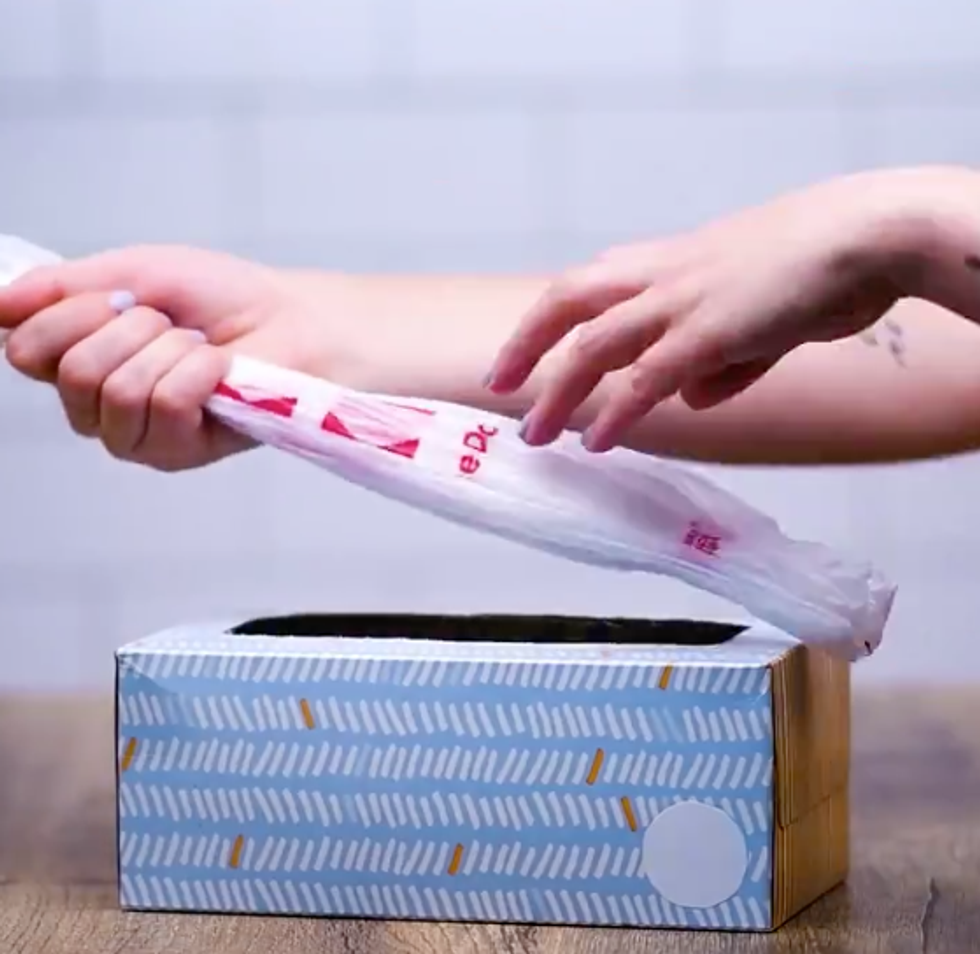Someone pushes a plastic bag into an empty tissue box